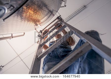 Female Winemaker Controls The Quality Of Wine On Ladder Over Tank