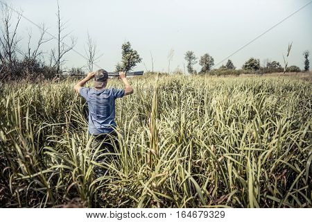 Hunter boy breaks through tall grass during hunting season in summer day with copy space