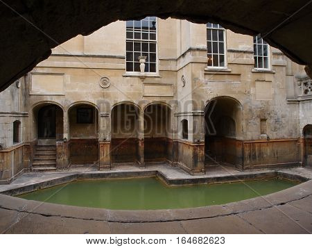 Tunnel leading to one of the Roman Baths in the city of Bath in England. The bath an surrounding architecture are cut from stone and include archways stairs and windows.