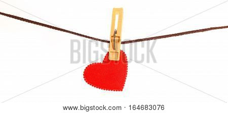 Red heart from dense fabric on a clothespeg on a rope. It is isolated on a white background