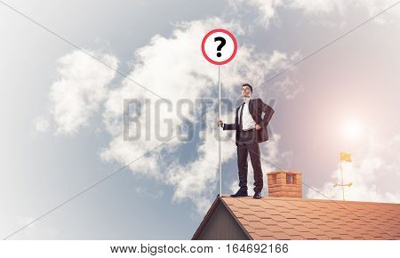 Young businessman with roadsign on roof edge. Mixed media