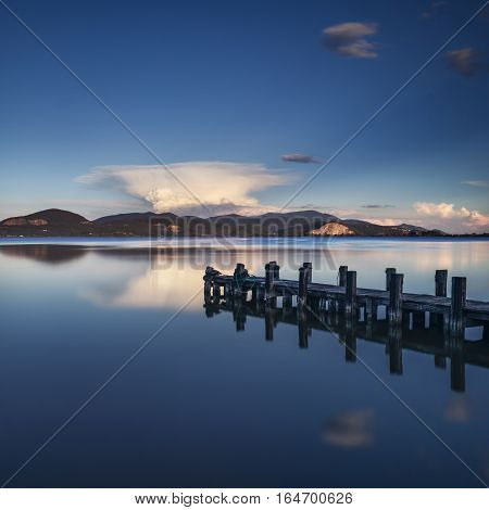 Wooden pier or jetty on blue lake sunset and sky reflection water. Long exposure Versilia Massaciuccoli Tuscany Italy.