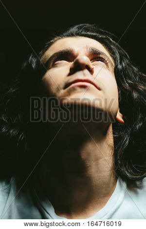Portrait of a handsome young man with long hair looks up closeup