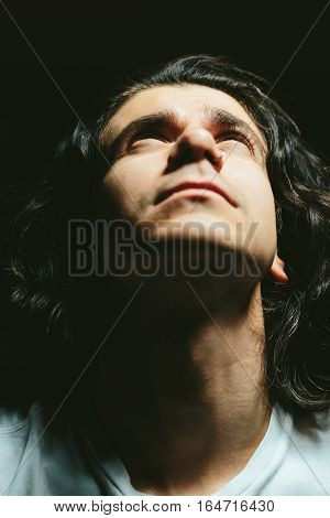 Portrait of a handsome young man with long hair looks up closeup