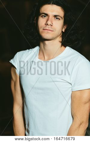 Portrait of a beautiful brutal guy with long hair on a dark background
