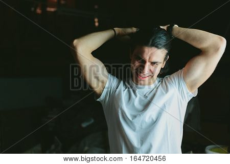 Beautiful long-haired brunette guy hands behind his head in white t-shirts