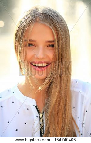 Pretty young woman or girl with long blonde hair in white blouse with stars and cute smiling face in sunny summer day