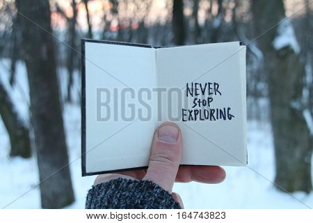 Never stop exploring. Inspirational and motivational quotes. Hand holding a book with the inscription.