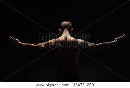 Unrecognizable man bodybuilder shows strong hands and neck muscles, athletic trapezius. Low key, studio shot on black background.