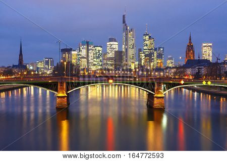 Picturesque view of Frankfurt am Main skyline and Ignatz Bubis Brucke bridge during evening blue hour with mirror reflections in the river, Germany