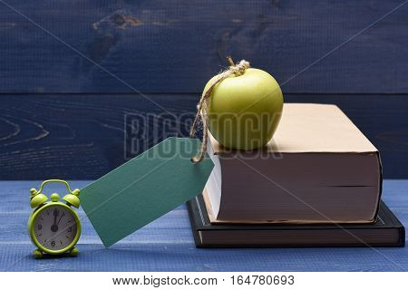 Books fresh green apple with turquoise tag string and alarm clock on blue vintage wooden background education concept copy space