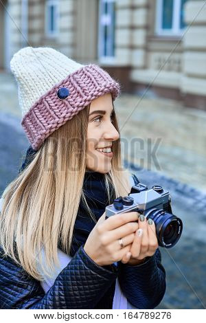 Beautiful girl photographer photographing the old town with retro camera. She is wearing a knitted cap