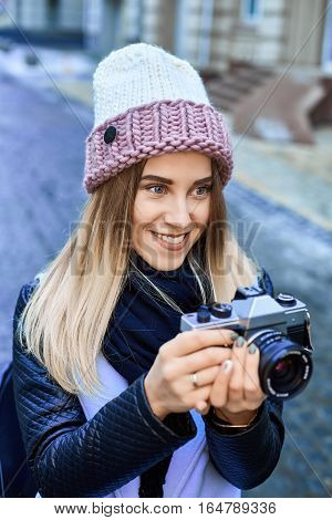 Beautiful girl photographer photographing the old town with retro camera. She is wearing a knitted cap