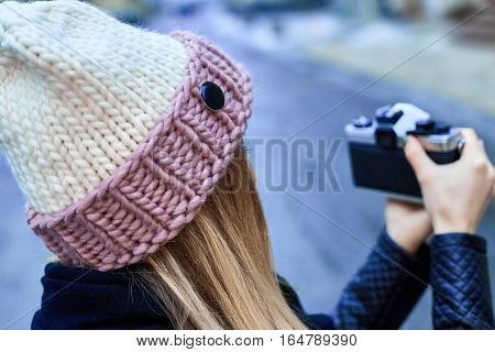 Beautiful girl photographer photographing the old town with retro camera. She is wearing a knitted cap