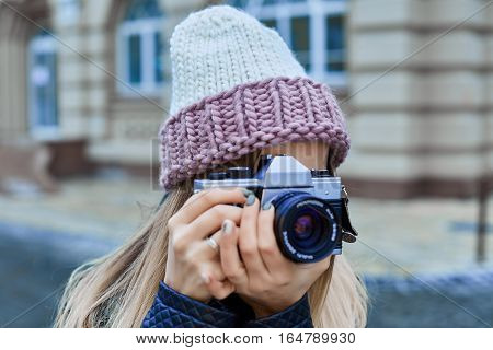 Beautiful girl photographer photographing the old town with retro camera. She is wearing a knitted cap