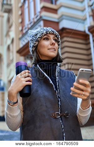 The girl with a smartphone and Thermocup, is walking through the old town