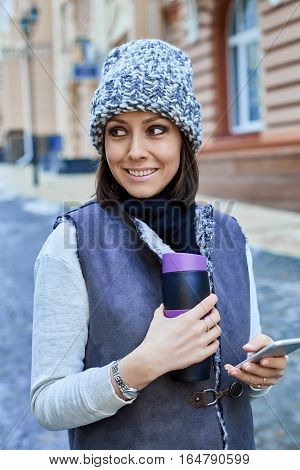 The girl with a smartphone and Thermocup, is walking through the old town