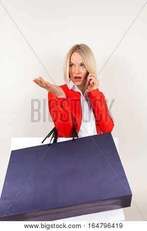 Portrait of young woman in a red jacket with shopping bags on a white background. Woman with shopping bags talking on the phone. Perturbation emotion