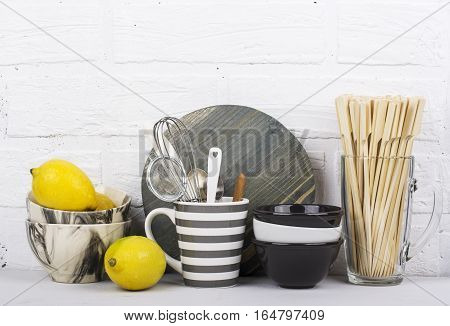Kitchen stylish modern trend still life monochrome colors, marble bowls, ceramic bowls, gray striped mug, wooden cutting board, juicy fresh lemons, kitchen tools on a background of a white brick wall. selective focus