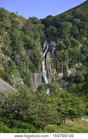 idyllic Tropical summer waterfall, distant portrait featuring trees, path, mountain side, clear blue sky