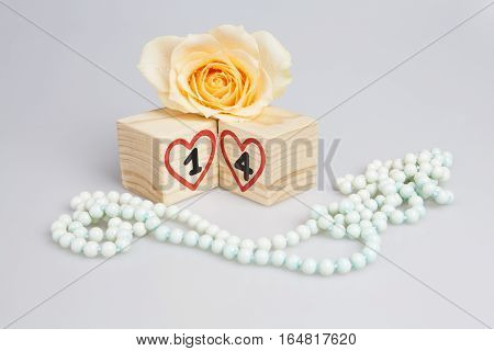 Wooden cubes with handwritten 14th and red hearts, yellow rose and beads.