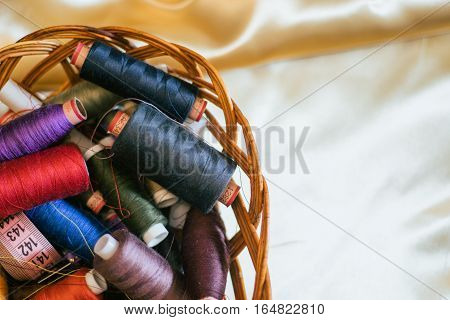 Vintage basket with sewing kit, multi-colored threads on fabric background