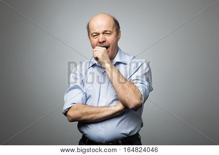 Bald man covers mouth with fist yawning with fatigue and sleepiness. Tired of the work and desire to sleep