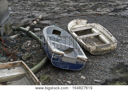 Two old beached wooden rowing boats white and blue, weathered and beaten on the shore