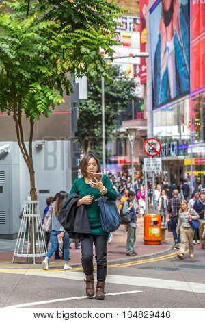 Hong Kong, China - December 6, 2016: a typical Asian woman writing with smart phone a message along Causaway Bay street market Jardine's Crescent, world famous for luxury shopping centers.
