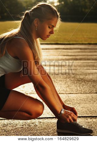 Athletic young brunette girl wearing in sportswear tying her running shoes and getting ready for jogging