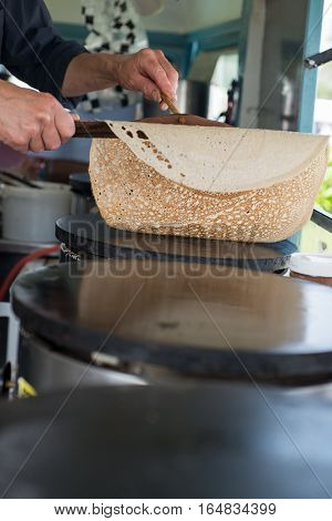 Hands flipping a crepe using wooden spreader and scraper