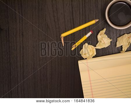 Dark surface yellow crumpled paper broken pencil coffee frustration