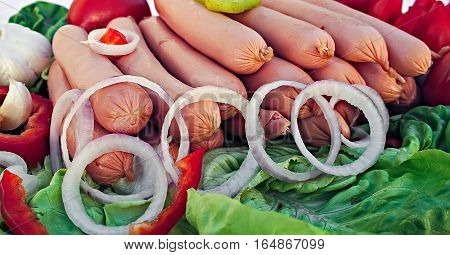 Sausages with onion rings, lettuce leaves, garlic and tomatoes.