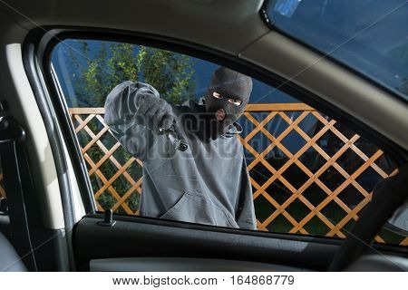 An armed man in the mask threatening pistol to the driver of the car