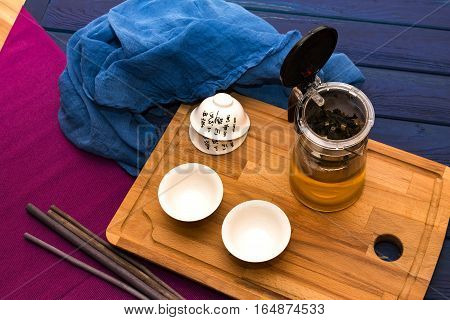 Green herbal tea in glass teapot on the blue wood background with aroma sticks and tea cup