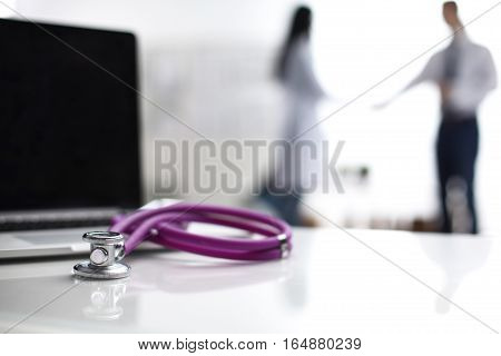 Laptop and stethoscope on the desk , doctors standing in the background.