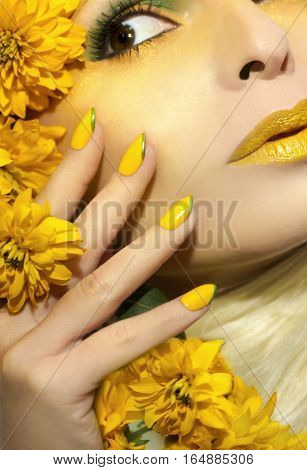Yellow makeup and manicure with a sharp oval shape of the nails on the woman with the flowers closeup.