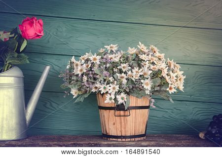 Beautiful flowers in wood bucket with pink rose on metal jug with vintage wood backround
