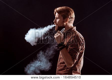 young man wearing a plaid shirt smokes an electronic cigarette on a black background