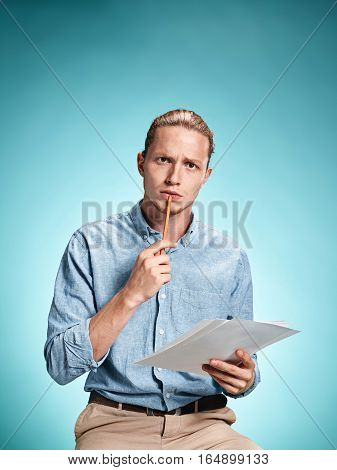 Smart sad student holding sheets of paper on blue studio background