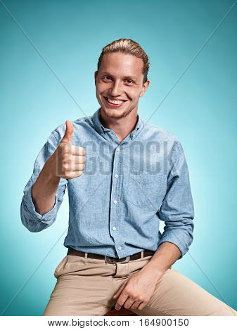 Happy excite young man in blue shirt smiling and celebrating his succcess over blue studio background