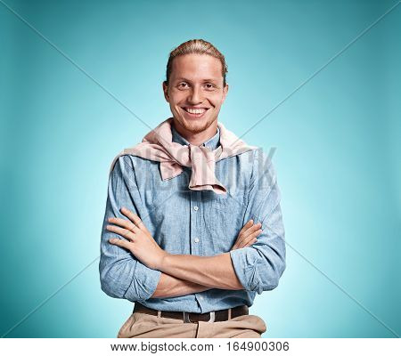 Happy excite young man in blue shirt smiling and celebrating his succcess over blue studio background