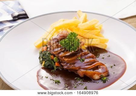 A nice dish of roasted duck breast confit in orange sauce served with fries on the table