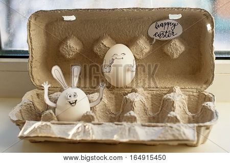 Two Easter smiling eggs in cardboard container. Egg-rabbit