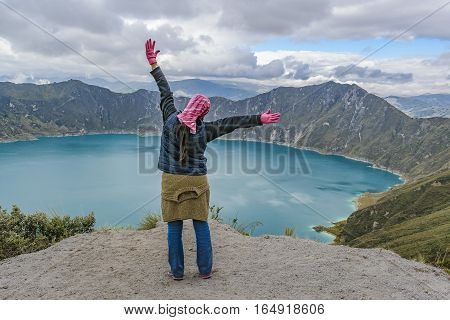 Young woman with hands up at watching the view at Quilotoa lake Latacunga Ecuador