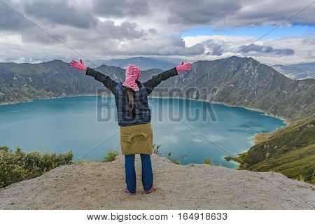 Young woman with hands up at watching the view at Quilotoa lake Latacunga Ecuador