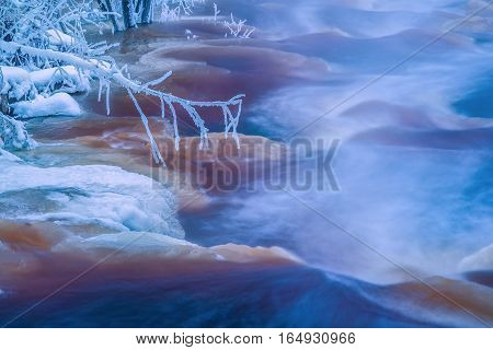 Frozen branch in cold winter stream landscape
