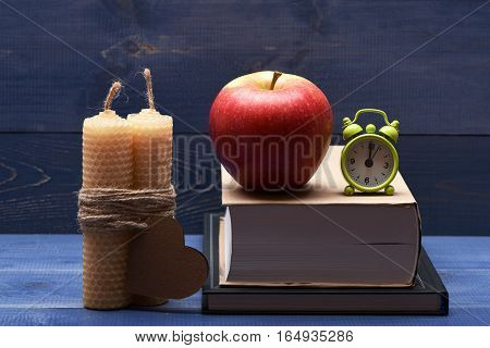 Decoration with fresh red apple candles with string valentine card books and green alarm clock on blue vintage wooden background valentine day concept