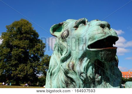 Rosenborg Palace in Copenhagen Denmark. Sculpture of lion against Rosenborg castle and blue sky. Statue is situated in front of bridge. Lion meditatively wistfully looking away.