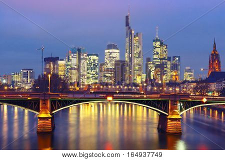 Picturesque view of Frankfurt am Main skyline and Ignatz Bubis Brucke bridge during evening blue hour with mirror reflections in the river, Germany